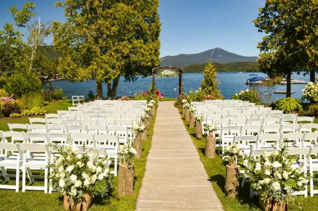 A picturesque outdoor eco friendly wedding ceremony set against a serene lake with mountains in the distance.