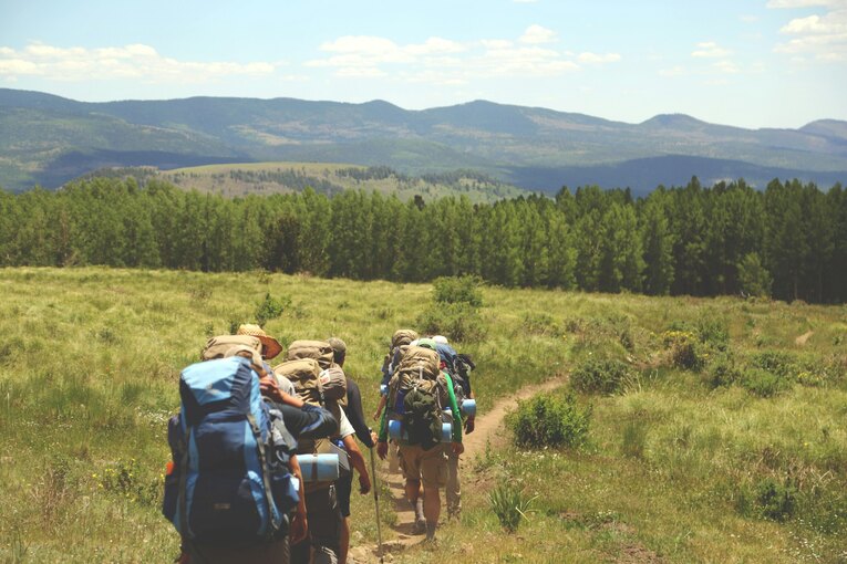 Each person is carrying a large backpack, suggesting a multi-day trek or backpacking trip, which is a great eco-friendly activity for students to engage in.